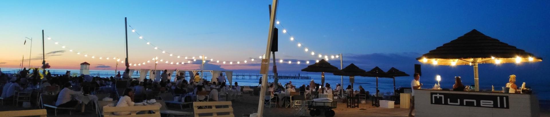 Spiaggia al tramonto con luci e bar Munell, persone rilassate.