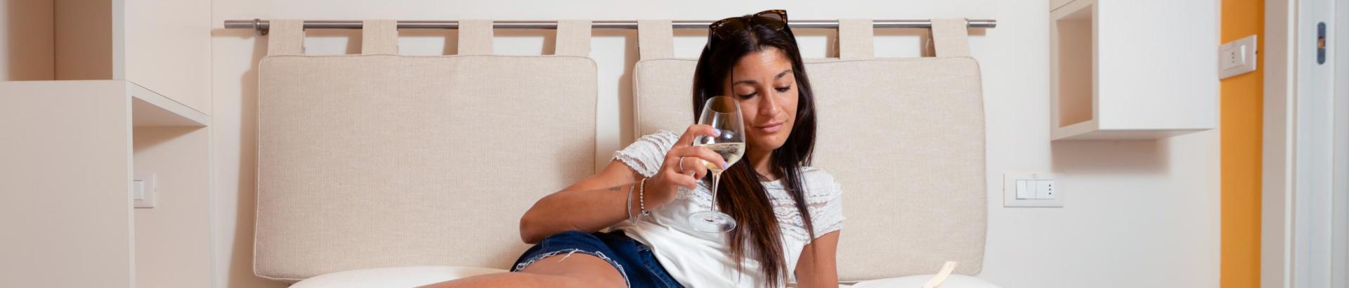 Relaxed woman reads a book and drinks wine on a bed.